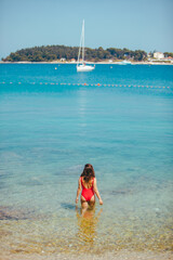 Wall Mural - sexy woman in red swimsuit standing in sea water. coastline yacht on background