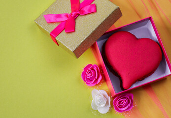 Wall Mural - box with hearts and roses.
A heart-shaped dessert maccaron lies in an open box on the right against a yellow background with decorative roses and a place for text on the left, a close-up top view.