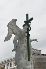 Wall Mural - Statue of a white stone angel holding a dark cross with a serpent or snake, on a grey day