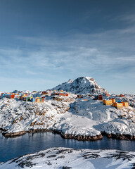 Wall Mural - a vertical shot of colorful houses on the snowy mountains near a frozen river in greenland
