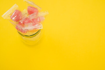 Sticker - A closeup shot of yummy candies in plastic bags in a jar isolated on a yellow background