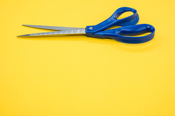 A closeup of metallic scissors on a yellow surface - space for text