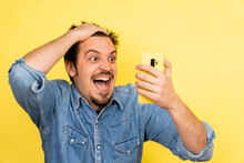 A Young Caucasian Male Showing Excitement After Seeing Something On The Phone Against A Yellow Background