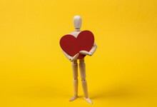 Wooden Puppet Holding A Heart On Yellow Background. Love, Valentine's Day Concept