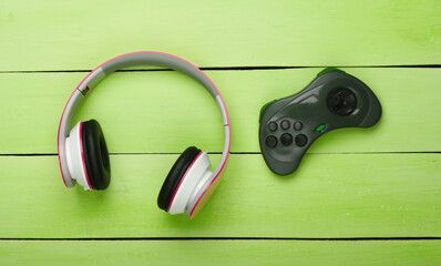 Canvas Print - Headphones and gamepad on green wooden background. Gaming, entertainment or leisure concept. Top view. Flat lay