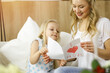 © rogerphoto - Happy mother day in sunny flat. Child daughter congratulates mom and gives her postcard with heart drawing. Family concept