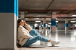 © Andrii  - Fashionable girl listening to music in wireless headphones while sitting in the underground parking of shopping mall