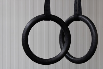 Detail of a set of black gymnastic rings or steady rings hanging in home gym over a white wall on the right side of frame. Empty space for text. Fitness or healthy lifestyle concept