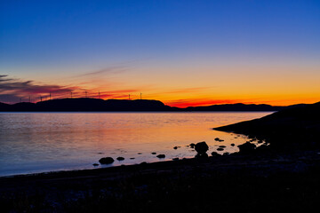 sunset over the sea with windmills on the mountain