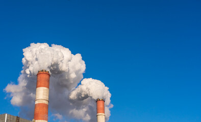 Powerful white puffs of smoke and steam from CHP chimneys contrast with the blue sky in December in Moscow