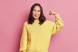 © wayhome.studio  - Horizontal shot of pretty Asian woman raises arms shows muscles being strong person has power dressed in casual yellow jumper poses against pink background. Look at my biceps after training.