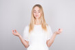 © Studio Nova - Calm, relaxed pretty blonde relieves stress, closes her eyes and smiles peacefully, meditating with her arms outstretched in mudra, Zen, standing in Lotus position, practicing yoga, gray background