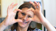 © Lsantilli - Smiling young woman showing hands sign heart shape looking at camera at home