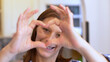 © Lsantilli - Smiling young woman showing hands sign heart shape looking at camera at home