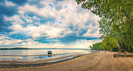 Wall Mural - dramatic autumn landscape with clouds, sandy river bank with fallen leaves. boat at the shore.