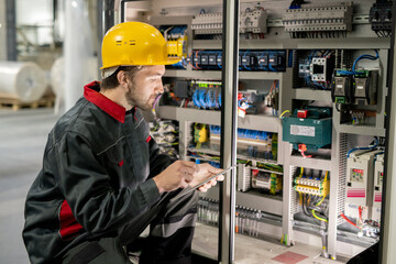 Poster - Contemporary young engineer in workwear and hardhat scrolling through data