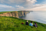 Fototapeta  - Girls sitting near the edge of the cliffs of Moher 