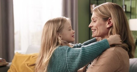 close up. side view of happy cute caucasian family mom and daughter sitting on couch hugging and pla