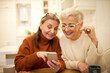 © shurkin_son - Two stylish retired female friends enjoying modern electronic gadget, sitting at cafe, watching pictures on mobile, recollecting good old days. Elderly women shopping online using smart phone