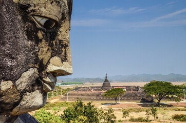 Sticker - A closeup shot of a stone statue face with temple on background in Mrauk U Myanmar