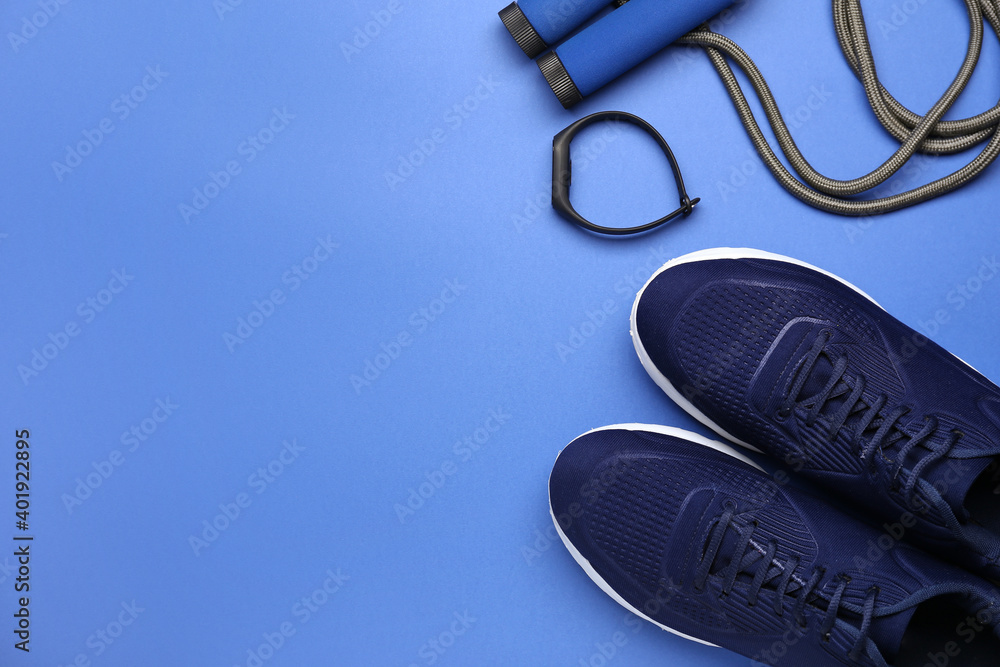 Sportive shoes and jumping rope on color background