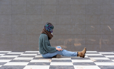 Poster - A closeup shot of a female in a facial mask sitting on a chess floor with a laptop - new normal concept