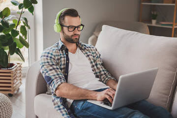 Poster - Profile side photo of young serious business man lie couch home remote work wear headphones watch seminar