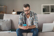 © deagreez - Photo of young man serious sit couch home look read browse internet cellphone wear casual outfit freelancer