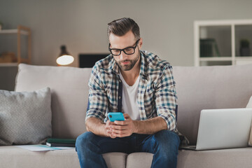 Photo of young man serious sit couch home look read browse internet cellphone wear casual outfit freelancer