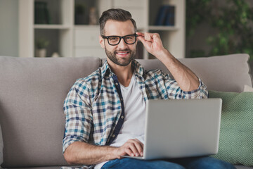 Poster - Photo of young handsome business man happy positive smile sit sofa home work distance browse laptop hand touch glasses