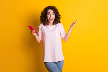 Sticker - Photo portrait of shocked woman with open mouth holding phone in one hand isolated on vivid yellow colored background