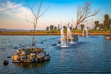 An artificial lake in the middle of the desert in UAE. Beautiful view of man-made lake and blue sky with green nature and water fountains.