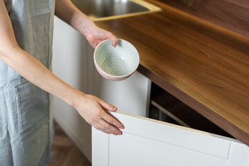 Wall Mural - Woman puts clean ceramic dishes in the cupboard