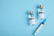 © New Africa - Vials with coronavirus vaccine and syringe on light blue background, flat lay. Space for text