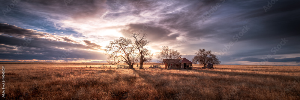 An old farmhouse on the eastern plains of Colorado in a rural setting at sunset. The sky is dramatic with wispy clouds. The old house if falling apart and abandoned.  - obrazy, fototapety, plakaty 