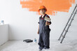 © Andrii Lysenko - a boy dressed in overalls and a protective helmet stands in the room holding a paintbrush in his hands. Home renovation concept.