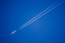 Looking Up At A Dutch KLM Twin Engine Jet Airliner In Deep Blue Sky With Vapour Trails Diagonally Across The Frame 