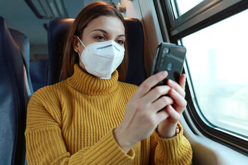 Relaxed woman with KN95 FFP2 face mask using smart phone app. Train passenger with protective mask traveling sitting in business class texting on mobile phone. Travel safely on public transport.