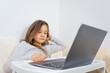 © QKon Studio - Emotional portrait of attractive cute girl 6-7 old she is tired in a bad mood sitting using laptop on distance learning