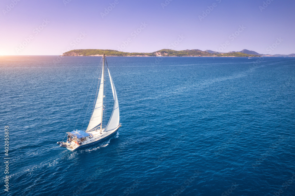 Aerial view of beautiful white sailboat in blue sea at bright sunny summer evening. Adriatic sea in Croatia. Landscape with yacht, mountains, transparent blue water, sky at sunset. Top view of boat - obrazy, fototapety, plakaty 