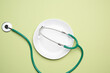© nndanko - round white ceramic plate and medical stethoscope on green background