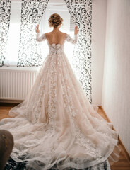 Wall Mural - A vertical shot of a bride wearing an elegant wedding dress and looking out of the window