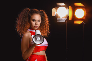 Poster - Beautiful young cheerleader with megaphone on dark background