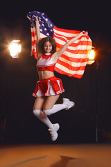 Poster - Beautiful young cheerleader with USA flag on dark background