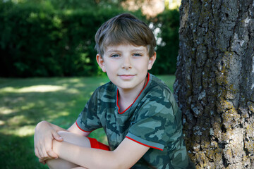 outdoor portrait of happy smiling preteen kid boy on sunny summer day in park near tree. handsome he