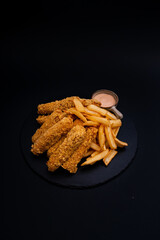 Canvas Print - A closeup shot of a tasty looking dish with fried chicken and fries isolated on a black background