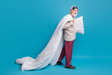 Poster - Full length profile side photo portrait of old man in eye mask walking with pillow blanket isolated on pastel blue colored background