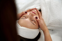 Of The Relaxed Spa Client During A Lifting Facial Massage In Beauty Salon. Close Up Portrait Of A Caucasian Beautiful Brunette Relaxing While Beautician Making A Lifting Massage To Her Face
