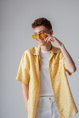 Young fashionable happy smiling man wearing trendy sunglasses, yellow shirt, white t-shirt, trousers. Summer fashion conception, studio portrait