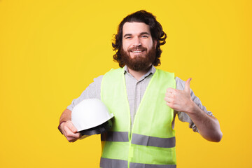 Wall Mural - Portrait of smiling bearded engineer holding white helmet and showing thumb up.